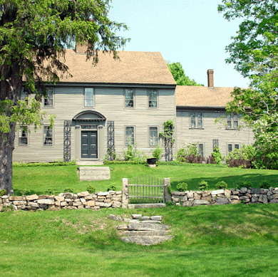 Front view of a two-story colonial house with addition or outbuilding and short stone wall with gate.